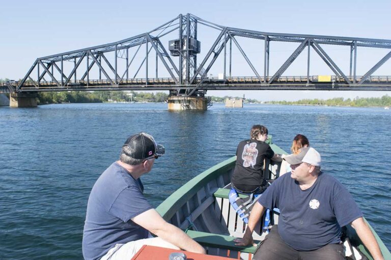 People on a wooden boat approaching the Little Current swing bridge.
