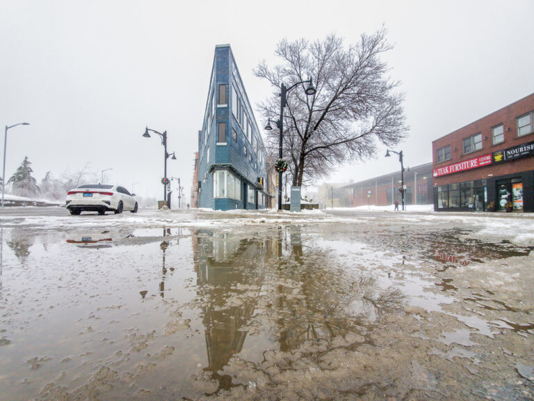 The flatiron building in Sudbury reflected in an icy puddle.