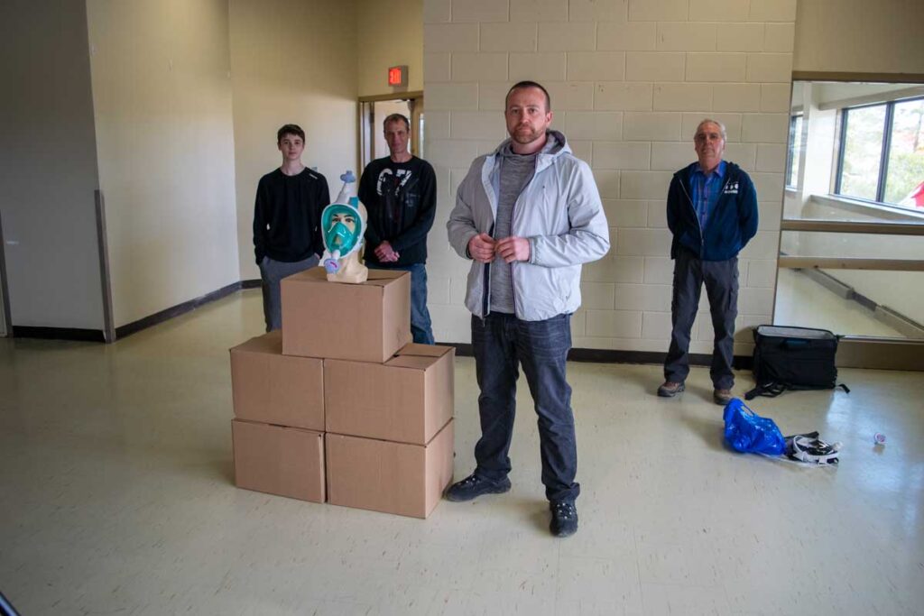Four men stand with boxes of oxygen snorkel masks.