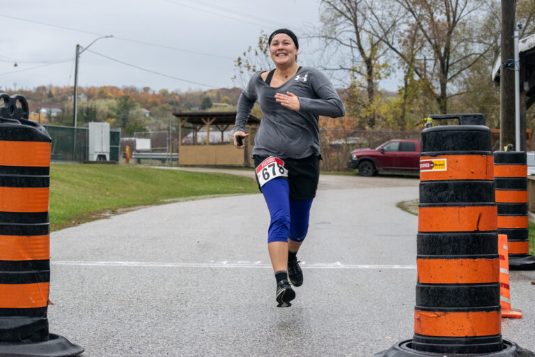 A woman runs straight toward the camera across a race finish line.