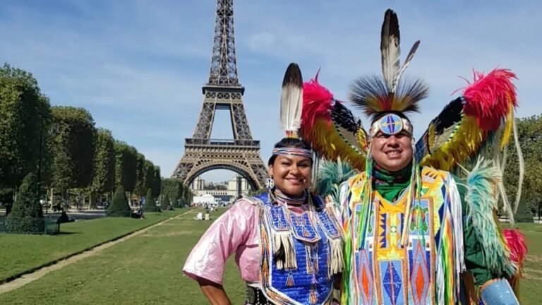 An Anishinaabe couple in regalia at the Eiffel Tower.