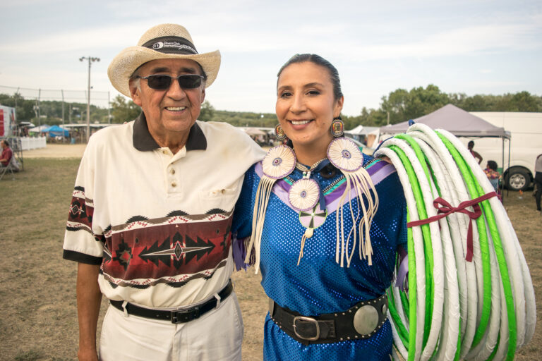 An old man and his daughter, an Indigenous hoop dancer, pose at a powwow.
